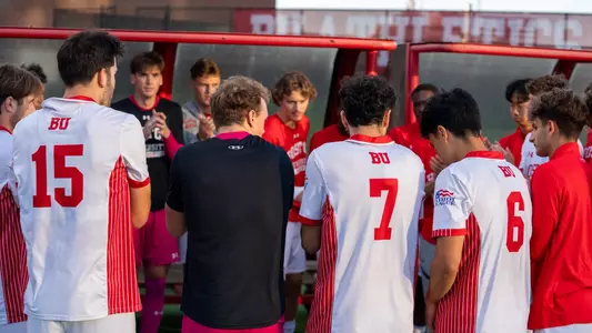 BU men's soccer team huddles up next to the bench