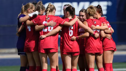 Photo of the BU Women's Soccer team huddling up before a game at UNH.