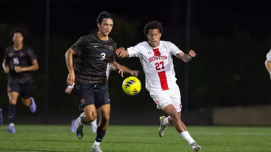 Austin Mobray runs up the field trying to reach the soccer ball with a Brown defender on his right side.