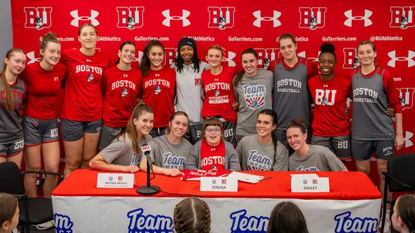 Photo of the BU Women's Basketball team posing for a photo with Team IMPACT signee Serena.