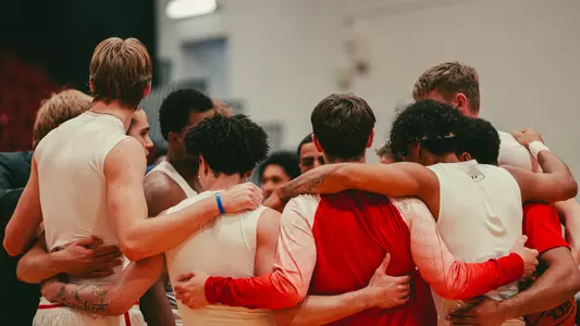 Men's Basketball players huddle together in a circle.