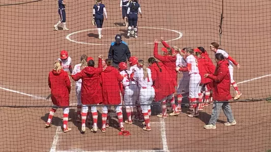 The softball players gather around home plate after Kyomi Apalit hit a home run at Bucknell.