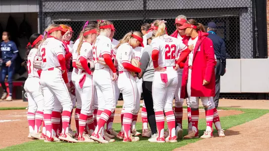 Softball team huddles at home in a circle.