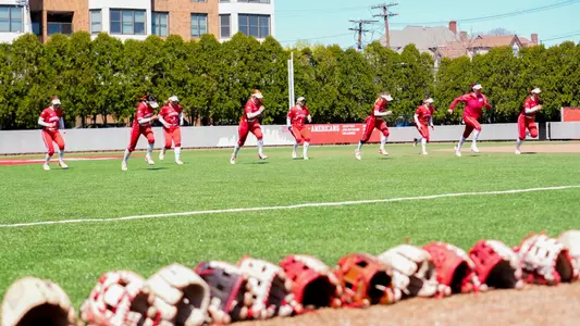 Softball players are warming up by participating in quick sprints at the home field.