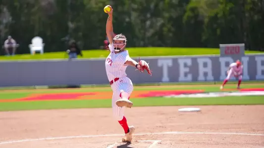 Kasey Ricard is in the middle of her pitching windup looking toward home plate against Bryant