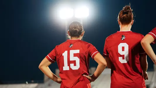Photo of women's soccer seniors Giulianna Gianino (left) and Margy Porta (right) in the starting lineup with their backs turned to the camera.