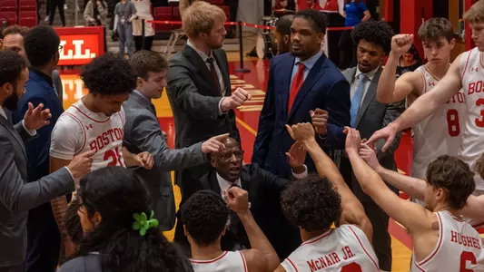 Men's basketball team members stick a closed fist into the middle of the huddle