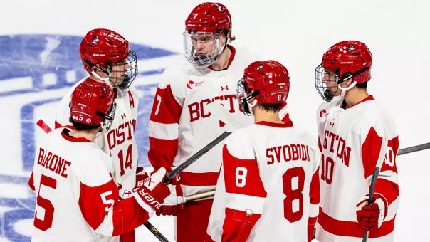 BU men's ice hockey players discuss something on the ice before a faceoff