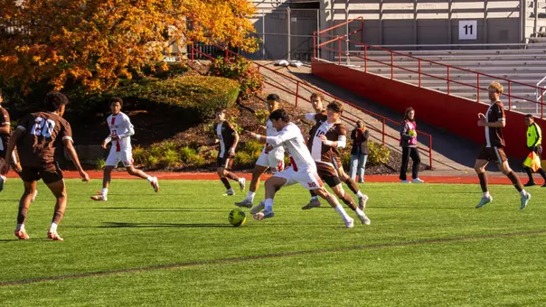 Men's Soccer player dribbles the ball up the field with multiple Brown defenders in front
