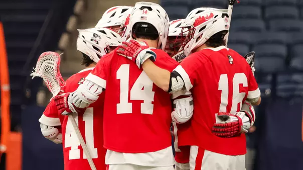 Men's lacrosse players huddle together in celebration