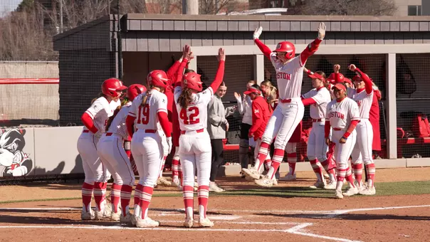 Kylie Doherty jumps high toward home plate with her teammates ready to embrace after a grand slam