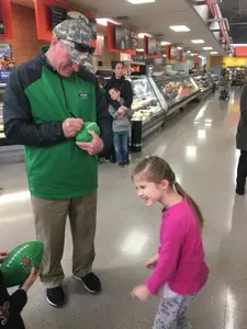 Doc Holliday signs a football for a young fan during the Marshall football team's annual toy drive at the Walmart in Barboursville.