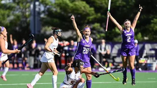 Skyler Brown raising first fist in the air with Puck Jansen jumping in the background as they celebrate a goal versus Central Michigan at the JMU Field Hockey Complex