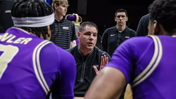 JMU men's basketball head coach Preston Spradlin leads a huddle during a timeout of a basketball game