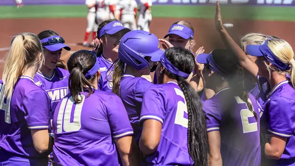 Softball players celebrating series win in a group hug.