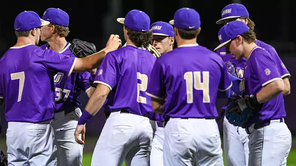 A group of JMU baseball players huddle together.