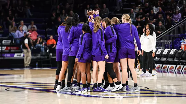 The women's basketball team putting their hands in together at midcourt of the Atlantic Union Bank Center