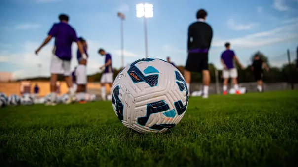 A soccer ball sitting on the ground at Sentara Park with players in the background.