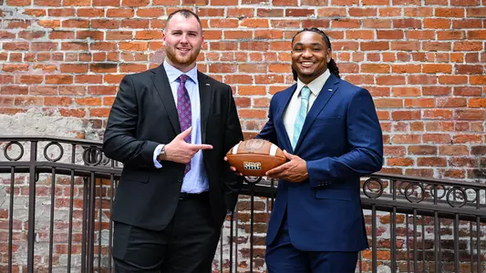 Zach Greenberg and Amar Thomas in suits in front of a brick wall during Sun Belt Media Day in New Orleans.