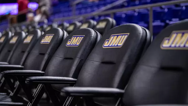 Shot of empty courtside seats displaying the JMU logo inside the Atlantic Union Bank Center.