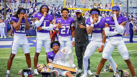Coach Barnes posing with players and the Battle of the Blue Ridge trophy after defeating Liberty at Bridgeforth Stadium.