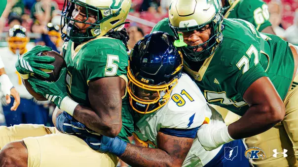Kent State defender (#91) tackling a USF ball carrier (#5) during a football game.