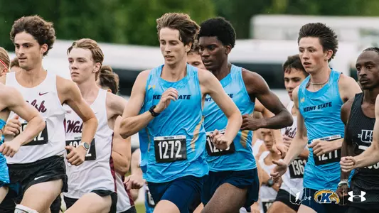 Kent State men's cross country runner in a light blue singlet with bib number 1272 runs near the front of a tightly packed group at the start of a race. Two Kent State teammates run beside him, surrounded by competitors in white Walsh uniforms and a black uniform.