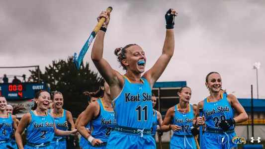 Torie Del Collo raising her hands and field hockey stick in the air as she and her teammates celebrate a win