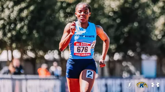 Kent State track and field athlete Grace Alls, in a light blue uniform and bib number 676, strides down the track at the NC State Raleigh Relays, focused and in full stride with a blurred background of trees and spectators.