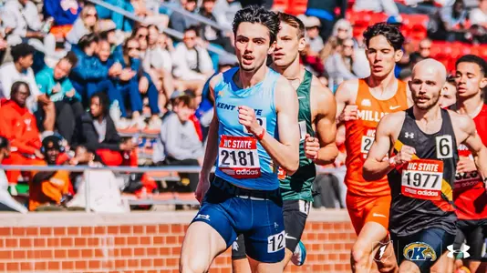 Kent State track and field athlete Evan Graessle, wearing bib number 2181, leads a pack of competitors at the Raleigh Relays, running in front of athletes from Michigan State, Millikin, and others with a full grandstand visible in the background.
