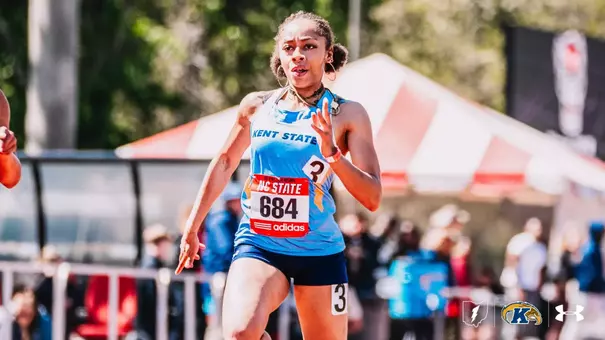Kent State University track and field athlete Laila Eiland, wearing bib number 684 and a light blue Kent State uniform, races during the NC State Raleigh Relays outdoor track meet. She wears the meet's adidas race bib over her uniform. Spectators and a tent structure are visible in the background. The Kent State Athletics logo and Under Armour wordmark appear in the lower right corner.