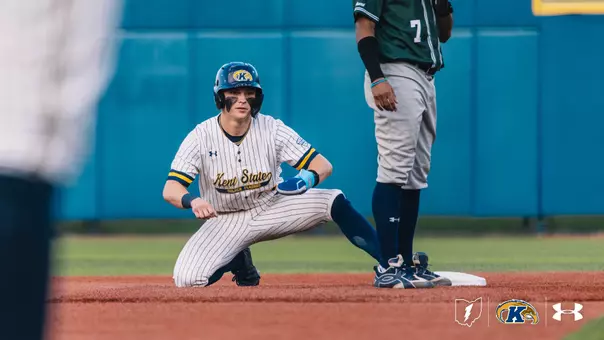 A Kent State Golden Flashes baserunner in a white pinstripe 'Kent State Golden Flashes' Under Armour jersey, navy socks, and a navy Golden Flashes batting helmet kneels at second base after a slide, with an opposing fielder in a green jersey and gray pants with No. 7 standing beside the bag.