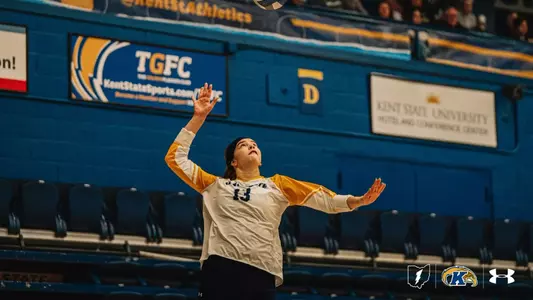 Kent State volleyball player Jordyn Anderson, wearing jersey No. 13, prepares to serve, eyes fixed on the ball as she reaches upward inside the MAC Center during a Golden Flashes home match.