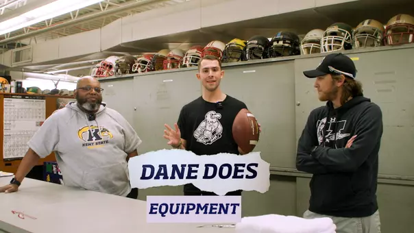 Dane Richardson stands in the equipment room with Cliff Ragin and Parker Kosh with football helmets on a cabinet behind them. Each person has kent state logos on their shirts