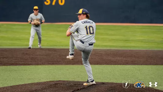Kent State Golden Flashes pitcher Ciaran Caughey, wearing No. 10 in a gray Under Armour jersey and gray pants, winds up in a high leg kick on the mound, with a teammate positioned in the infield behind him and the outfield wall with the distance marker '370' visible in the background.