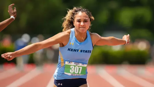 Kent State sprinter Amryne Chilton (bib 307) leans across the finish line with arms spread wide during the MAC Outdoor Track and Field Championships.