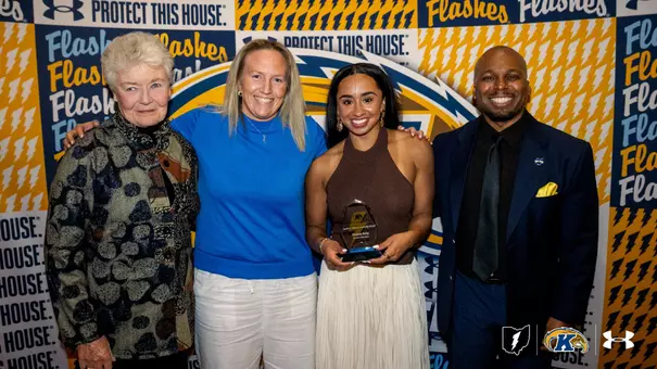 Dionna Gray of Kent State women's basketball holds the Judith V. Devine Leadership Award at the Devine Dinner, posing with three others in front of a Kent State Golden Flashes step-and-repeat backdrop.