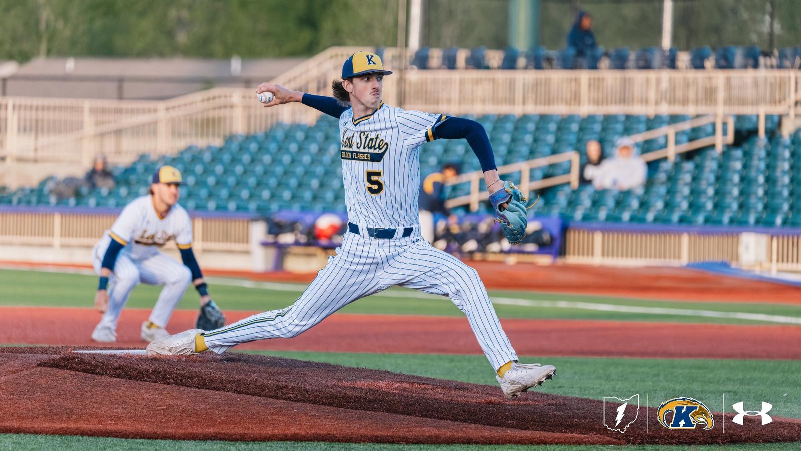Kent State Golden Flashes pitcher wearing No. 5 extends fully through his delivery on the mound in a white pinstripe 'Kent State Golden Flashes' Under Armour jersey, navy sleeves, and a navy gold-brimmed cap, with a teal glove, a teammate set at an infield position behind him, and a partially filled