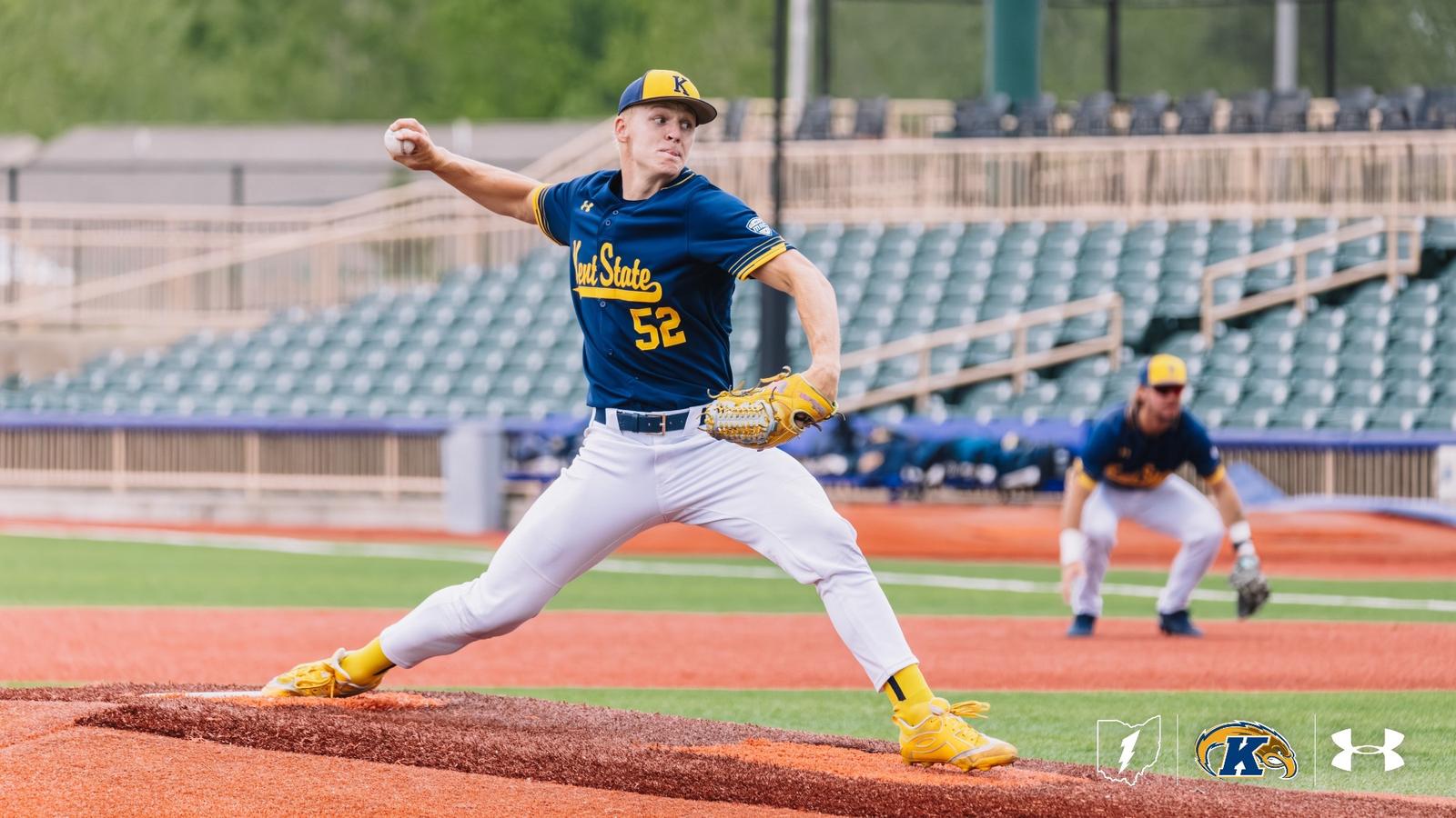 Kent State Golden Flashes pitcher wearing No. 52 extends fully through his delivery on the mound in a navy 'Kent State' Under Armour jersey, white pants, gold cleats and socks, and a navy gold-brimmed cap, with a gold glove, a teammate set at an infield position behind him, and a partially filled st
