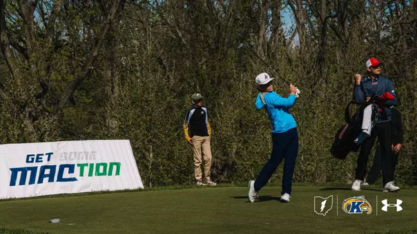 Kent State golfer Liam Curtis follows through on his swing wearing a bright blue pullover and white cap, with his caddie standing to his right and a "Get Some MAC-tion" banner visible behind him on the tee box.