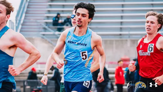 Kent State track and field athlete Evan Graessle, wearing a light blue Under Armour uniform with "Kent State" across the chest and bib number 5, runs during a middle-distance event at the OSU Invitational, surrounded by competitors including a Miami (Ohio) runner in red with bib number 6. The Kent State Athletics logo and Under Armour wordmark appear in the bottom right corner.
