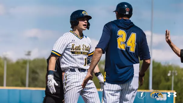 Kent State Golden Flashes player No. 14 in a white pinstripe 'Kent State Golden Flashes' Under Armour jersey is greeted near home plate by a Kent State coach wearing No. 24 in a navy jersey, with a hand extended for a high five visible at right and a partly cloudy sky in the background.