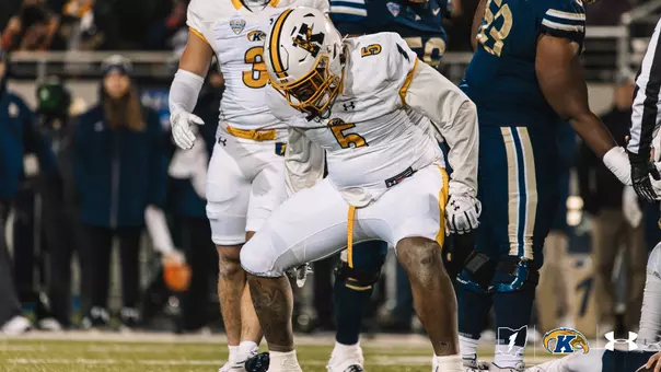 A Kent State football player wearing a white jersey with the number 5 and a white helmet stands on the field during a night game, looking down in a slightly crouched stance.