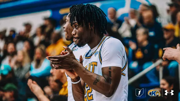 Kent State Men's Basketball player #22 Jaymen Townsend claps his hands in a white home jersey while on the court, with teammates and a crowd of fans cheering in the blurred background. The Kent State, and Under Armour logos appear in the bottom right corner.