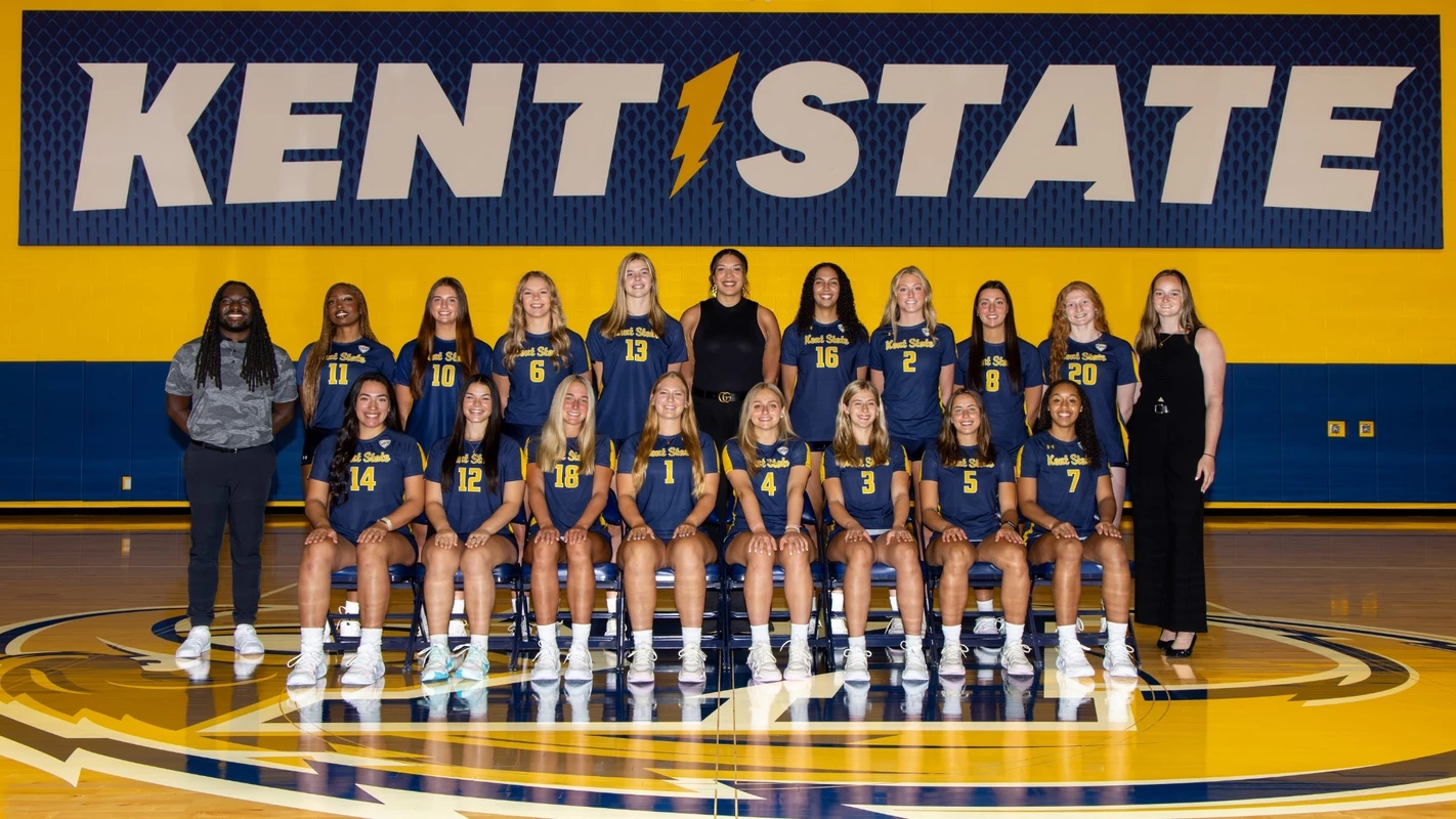 Kent State volleyball team photo. Two rows pose in front of a gold and navy 'Kent State' wall banner on the court.