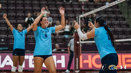 Kent State volleyball players celebrate on the court in front of a mostly empty arena during a match against Virginia Tech.
