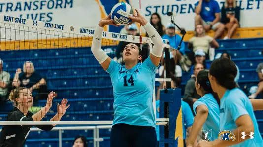 Kent State setter (#14) sets the ball at the net, with a Cleveland State blocker reaching up and Kent State teammates nearby.