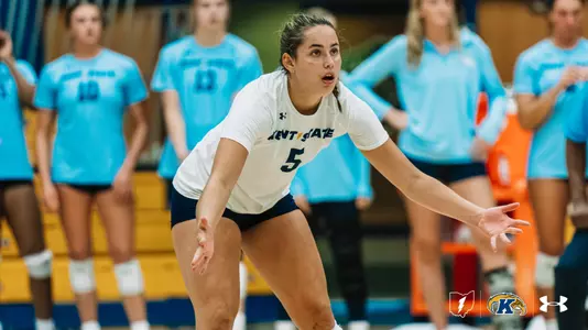 Kent State libero No. 5, wearing white, shuffles into defensive position with arms out, focused on the play in front of her.