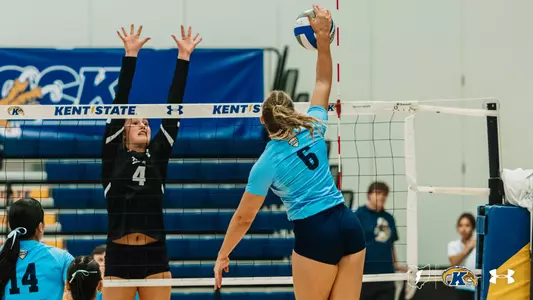 Kent State player (#6) sets the ball at the net against a Cleveland State blocker (#4) reaching up in defense.