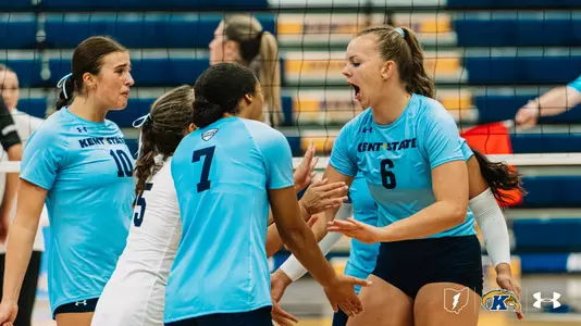 Kent State players (#10, #5, #7, #6) celebrate together at the net after scoring a point.